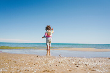 Fototapeta na wymiar Wide view of a little girl wearing rainbow hoodie playing at the beach