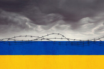 Muro con i colori della bandiera ucraina recintato da filo spinato sotto un cielo tempestoso.