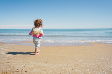 Wide view of a little girl wearing rainbow hoodie playing at the beach