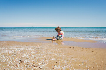 Fototapeta na wymiar Wide view of a little girl wearing rainbow hoodie playing at the beach