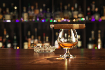 close up view of cigar and glass of cognac on color back. 