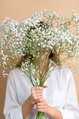 people and floral design concept - portrait of woman holding bunch of gypsophila flowers over beige background