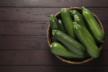 Raw ripe zucchinis in wicker bowl on wooden table, top view. Space for text