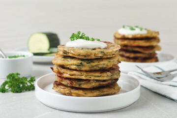 Delicious zucchini pancakes with sour cream served on light grey table