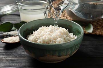 Pouring water into bowl with rice on wooden table