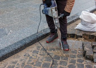 A male worker repairs the pavement with a jackhammer. The work of the municipal service