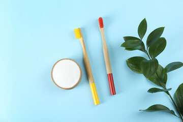 Bamboo toothbrushes and bowl of baking soda on light blue background, flat lay