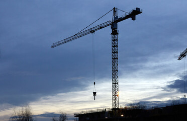 Budowa apartamentowca z dźwigiem budowlanym podczas budowy na tle błękitnego wieczornego nieba z chmurami