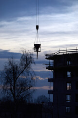 Budowa apartamentowca z dźwigiem budowlanym podczas budowy na tle błękitnego wieczornego nieba z chmurami