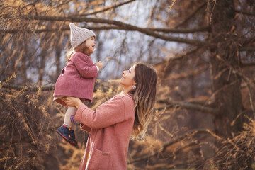 Beautiful young mother with her little daughter in park. Mother kissing her child outdoors. Family playing in autumn park.