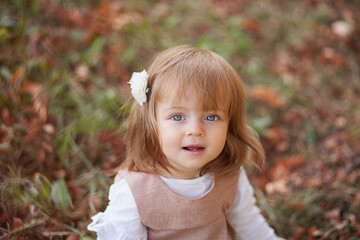 Fototapeta premium Little beautiful girl portrait in autumn street. Happy smart small girl in autumn park