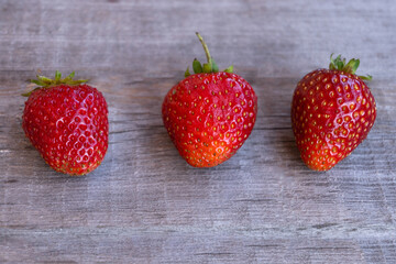 Three ripe strawberries lie on a wooden surface. Summer, strawberry season.