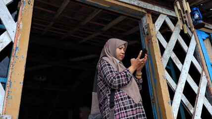 a woman wearing a hijab while using her phone to send news