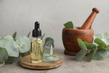 Bottle of eucalyptus essential oil, plant branches, wooden mortar and pestle on grey table