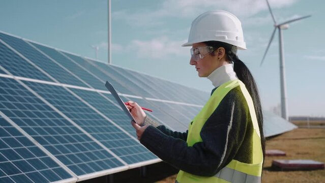 Close up of female ecological engineer checking the operation of solar panels. Environment engineer works at the power station, wearing safety vest, recording information. High quality 4k footage