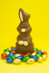 Easter. A chocolate bunny on a yellow background and colorful eggs and sweets are scattered around. Holiday concept, promotions, sale, gifts, discounts mockup