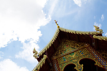 roof of a thai temple with ornaments and blue sky with clouds