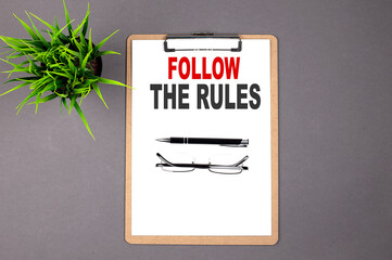 Text FOLLOW THE RULES on the brown clipboard on the grey background. Business concept