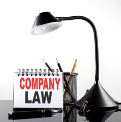 COMPANY LAW text on notebook with pen and table lamp on the black background