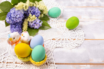 Fototapeta na wymiar Easter composition with multi-colored eggs in a ceramic stand-rabbit and a spring bouquet with purple and yellow flowers on a hand-knitted napkin, copy space, flat disign