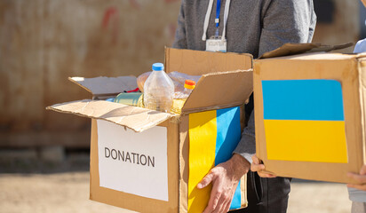 Close up photo of volunteer carrying box with humanitarian aid for ukrainian refugees in street,...
