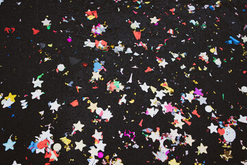 Party Poppers. Colorful explosion of holographic multicolored confetti lying scattered on a black surface. Bright multicolored tinsel, glitter, stars texture top view. Festive decoration background.