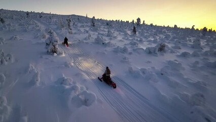 Aerial drone view tracking snow sleds climbing a steep fell, winter sunset in Lapland - Powered by Adobe