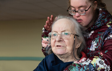 Daughter with Down Syndrome holding her senior mother, sitting in a wheel chair