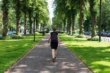 Fototapeta premium Attractive woman in black dress walking in a green city park