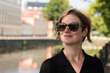 Portrait of a thirty year old pritty white woman with a black dress and sunglasses in a city park environment