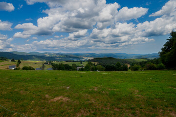 Naklejka premium The green meadow the hills and the blue sky. The Vosges mountains in France, with green meadows forest some clouds and the blue sky.