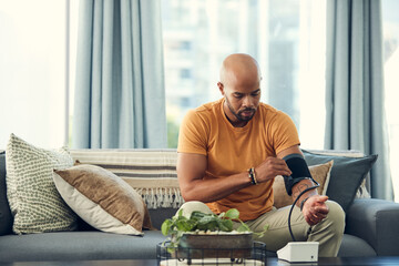 Im experiencing headaches so my blood pressure might be high. Shot of a young man taking his blood pressure while sitting on the sofa at home.