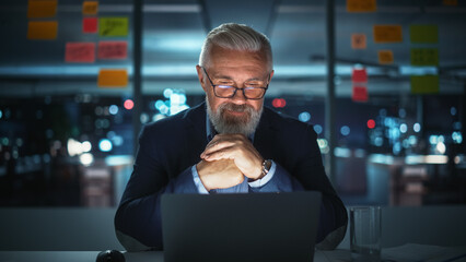 Successful Senior Businessman Working on Laptop Computer in Big City Office Late in the Evening. Investment Analyst Checking Financial Management Reports, Working with Documents