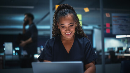 Portrait of African American Businesswoman Working on Laptop Computer in Big City Office Late in...