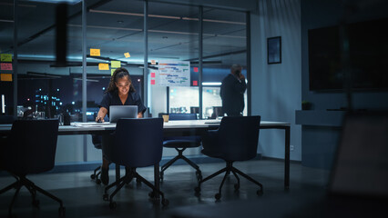 Portrait of African American Businesswoman Working on Laptop Computer in Big City Office Late in the Evening. Female Executive Director Managing Digital e-Commerce Project, Finance Analysis