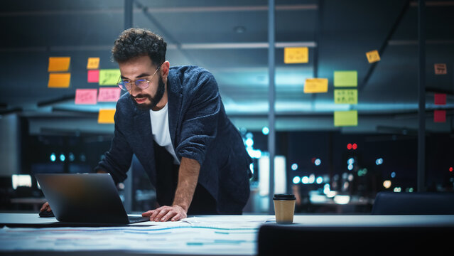 Successful Handsome Creative Director Working on Laptop Computer in Big City Office Late in the Evening. Businessman Preparing for a Marketing Plan in Conference Room.