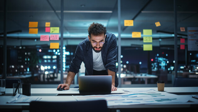 Successful Handsome Creative Director Working on Laptop Computer in Big City Office Late in the Evening. Businessman Preparing for a Marketing Plan in Conference Room.