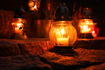 Different grave lanterns with burning candles on stone surface at night
