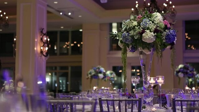 Wedding banquette floral center pieces with purple pink and white roses carnations and hydrangeas with accent evening lighting