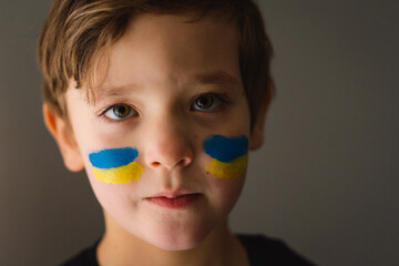 Portrait of a Ukrainian boy with a face painted with the colors of the Ukrainian flag. Ukrainian boy asks to stop the war in Ukraine. War of Russia against Ukraine.