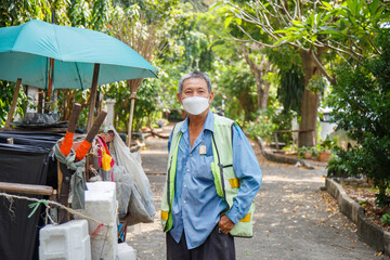 Portrait happy old Asian man street cleaner wearing a masks pick a pocket next to an old gabage...