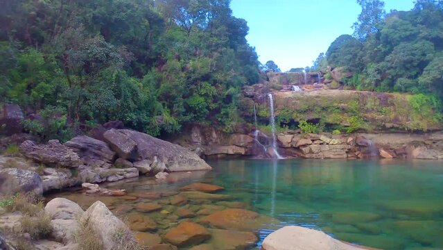natural waterfall falling from mountain top with dramatic blue sky at forests