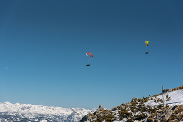 paraglider in front of snows alpine mountain range with clear blue sky