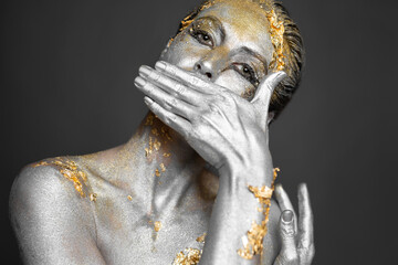 Portrait of a beautiful female model with gold and silver paint on her skin and hair in the studio.