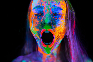 Beautiful young woman in neon light. Portrait of a model with fluorescent makeup who poses in UV light and screams