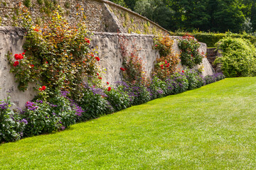 Parterre de fleurs d'été au pied d'un vieux mur en pierre devant une pelouse verte