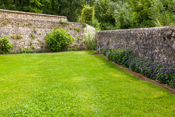 Parterre de fleurs d'été au pied d'un vieux mur en pierre devant une pelouse verte
