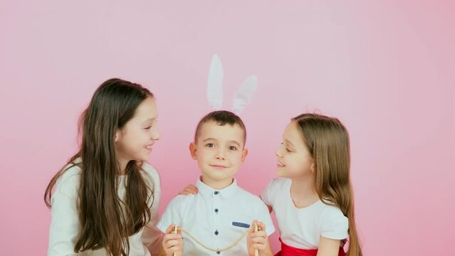 Little boy wearing bunny ears holding basket and is kissed on cheek by histwo sisters, Easter holiday concept.