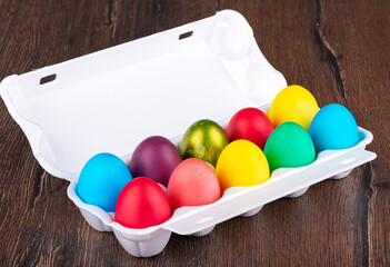 Multi-colored Easter eggs in a white plastic package on a wooden background.