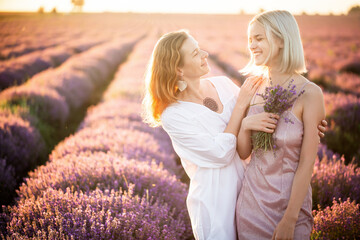Mom and daughter are standing together in a purple lavender field. The friendly relationship of a teenage girl and a mother of a woman in transition. Two women communicate and smile at each other.